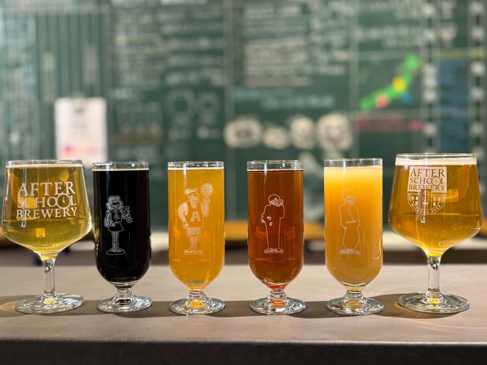 カウンターに、色の異なる6杯のクラフトビールがグラスに注がれて並んでいる。グラスには「AFTER SCHOOL BREWERY」の文字とイラスト。
