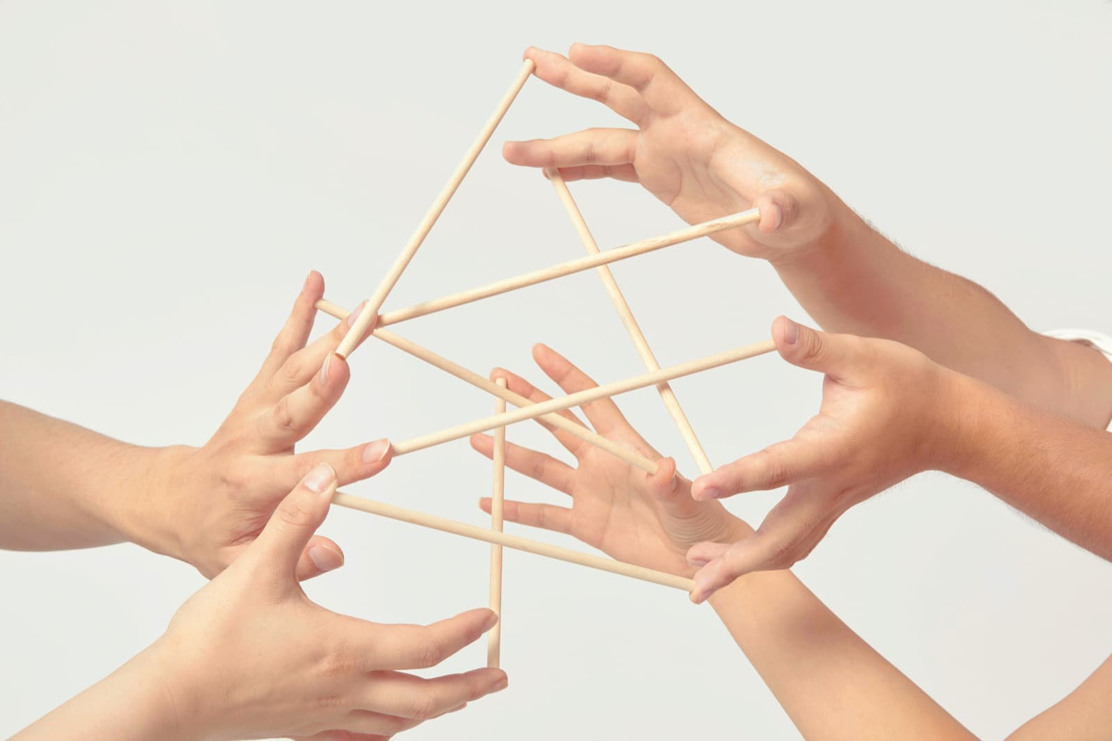 5人の手が集まり、指先どうしを細い木の棒でつなぎ合って、棒を落とさないよう支えている。
